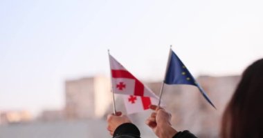 Kadın şehir caddesinde Gürcü ve Avrupa Birliği bayrakları sallıyor. Güçlü ortaklık kavramı ve işbirlikçi diplomatik bağlantı yavaş çekim
