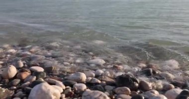 Huzurlu ve sakin bir sahil sahnesi. Yumuşak okyanus dalgalarının yanında pürüzsüz çakıl taşları dizisi.