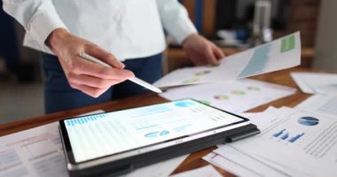 Bir profesyonel, çeşitli yazılı raporlar ve belgelerle çevriliyken bir tablet üzerindeki verileri özenle analiz eder.
