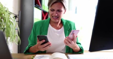 Karışık masasındaki bir kadın iki akıllı telefonu aynı anda idare ederken derin hayal kırıklığını ifade ediyor.