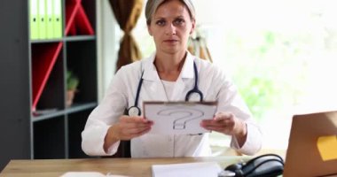 Belirgin bir soru işareti olan ve belirsizliğini gösteren bir tabela tutan bir doktor oldukça şaşkın görünüyor.