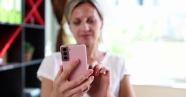 Bir kadın canlı pembe akıllı telefonuna derinden odaklanır, tamamen şık ve parlak bir çevreye dalmıştır.
