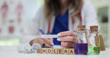 Kendini adamış bir sağlık uzmanı kolerayı inceliyor. Gelişmiş laboratuvar ekipmanları ve çeşitli şişeler kullanıyor.