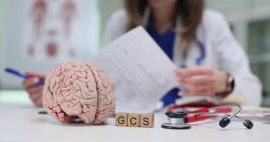 Kendini adamış bir sağlık çalışanı önemli GCS değerlendirme belgeleriyle birlikte detaylı bir beyin modeli üzerinde çalışıyor.