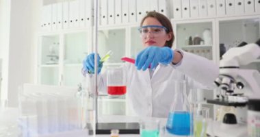 Profesyonel kadın bilim adamı, beher kabının içindeki kırmızı sıvıya dikkatlice reaktör ekliyor. Teknisyen kesin bir laboratuvar deneyi yürütüyor.