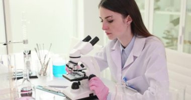 Kadın laboratuvar teknisyeni biyolojik örnekleri mikroskopla inceliyor. Genç kimyager, profesyonel bilim ortamında numunelerle çalışıyor.