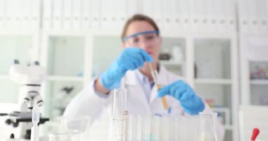 Kadın araştırmacı laboratuarda cam sondayla test tüplerinde sıvı karıştırıyor. Kadın laboratuvarda bilimsel analiz yürütüyor ve ağır çekimde çalışıyor.