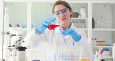 Kadın bilim adamı kırmızı sıvıyı laboratuvar bardakları arasında aktarıyor. Tıbbi kimyager araştırma tesisinde kesin kimyasal analizler yapar.