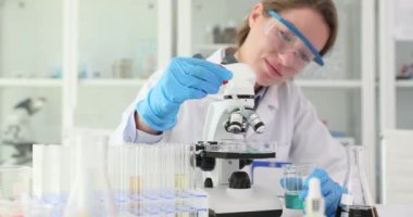 Profesyonel bilim adamı laboratuvarda numuneyi mikroskop altında analiz eder. Kadın biyolog, Petri kabında renkli kimyasallarla deney yapıyor.