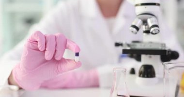 Bilim adamı laboratuarda mikroskop yakınında deneysel ilaç kapsülü tutuyor. Eczacı tıbbi laboratuvar ortamında yenilikçi maddeleri test ediyor