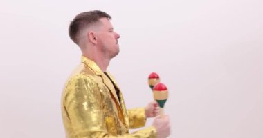 Altın ceketli enerjik müzisyen beyaz arka planda marakas çalar. Latin kültürü dans partisinde canlı ritmik müzikal performans