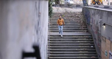 Genç adam kirli yeraltı geçidine çıkan merdivenlerden iniyor. Sarı ceketli adam ağır çekimde karşıya geçmek için güvenli bir yol seçti.