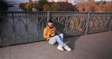 Şehrin kaldırımlarında oturan modern dizüstü bilgisayardaki neşeli serbest çalışan tipler. Gülümseyen erkek, günbatımının ufuk çizgisini nefes kesici bir şekilde seyretmekten hoşlanır. Yavaş çekim