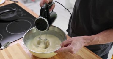 Profesyonel pasta şefi dikkatli bir şekilde kek hamuru çırpıyor. Pasta aşçısı büyük karıştırma kabındaki malzemeleri karıştırmak için elektrikli mikser kullanır. Yavaş çekim