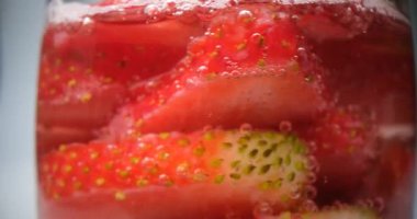 Taze dilimlenmiş çilekler temiz bir bardak suda yüzer. Restoranda serin ve ferahlatıcı bir kokteyl yapmak için hazırlanmış çilek dilimleri.