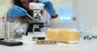 Kendini işine adamış bir bilim adamı, odaklanmış bir laboratuvar ortamında mikroskop altında çeşitli ilaçları dikkatle inceliyor.