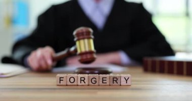 Profesyonel yargıç sahtecilik davasını sonuçlandırmaya dikkat ediyor. Tahta küpler yargıç masasında ForGERY sözcüğü oluşturur. Yavaş çekim