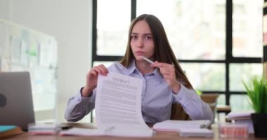 Yorgun kadın ofis çalışanı kalemle kontratı işaret ediyor. Genç, uzun saçlı iş kadını, iş ortağını belge imzalamaya teşvik ediyor. Yavaş çekim