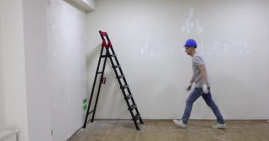 İnşaat işçisi odada yüksek alüminyum merdiven çıkıyor. Sert şapkalı ve temiz koruyucu gözlüklü biri sağlam bir merdiven tırmanır. Yavaş çekim