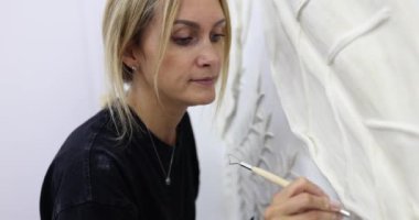 Konsantre kadın refakatçi, özel bıçakla zarif bas-rahatlatmayı yeniliyor. Tasarımcı, müzede ustalıkla sıva sanatını muhafaza ediyor.