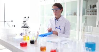 Profesyonel kadın bilim adamı kimyasal deney için koruyucu mavi eldivenler giyer. Kimyager gelişmiş mikroskop yakınlarındaki sıvıları analiz eder.