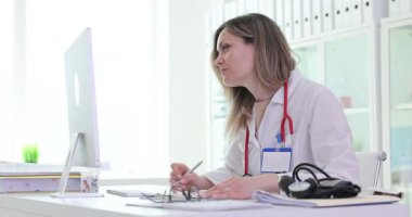 Kadın sıhhiye klinikteki fazla veriyi görmezden gelerek bilgisayardaki belgeleri analiz ediyor. Kadın doktor ofiste dijital dosyaları okuyarak hasta kayıtlarını dolduruyor.