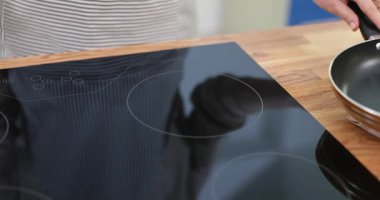 Mutfak uzmanı pozisyonları paslanmaz tavayı şık indüksiyon sobanın üstüne koyuyor. Kadın mutfakta kesin yemek hazırlama işlemini başlatıyor.