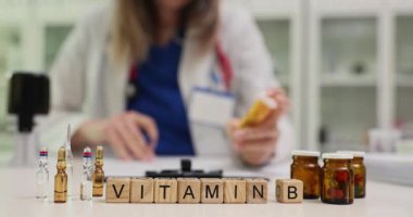 B vitamini. Doktor masasında şişe ve tüpler var. Kadın terapist, doz ve sağlık stratejilerini tartışan ek faydaları anlatıyor