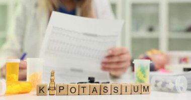 K vitamini ve Potasyum 'u tıbbi profesyonel iş yerine yerleştirilmiş küplere yaz. Doktor, çeşitli ilaçlarla masada oturan hastaların kayıtlarını inceler.