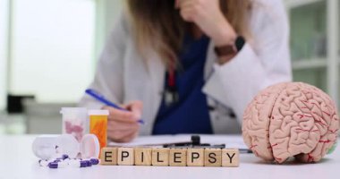 Doktor masasında epilepsi ve beyin anatomik modeli var. Tıbbi uzman klinik bürosunda yavaş çekimde reçete yazıyor.