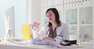 Kadın doktor, klinikteki işyerinde yorgunluktan yorgun düşen alnına dokunuyor. Doktor hasta geçmişiyle uğraşmaktan yoruldu.
