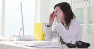 Kadın doktor bilgisayar ekranına bakarken gözlüğünü çıkartıyor. Üniformalı kadın doktor, ağır çekimde neşe ve kızgınlık ifade ediyor.