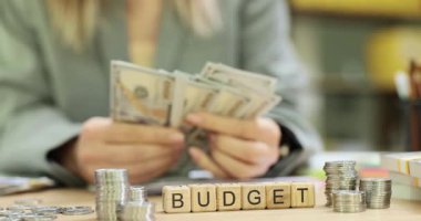 Minyatür tahta bloklar masada kelime bütçesi oluşturur. Kadın, hesaplamaları iki kez kontrol eden kalın banknotlar sayıyor. Yavaş çekim