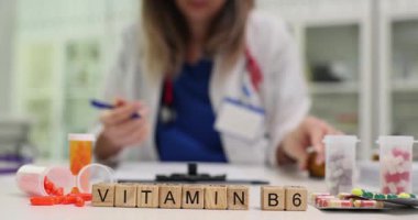 Profesyonel kadın doktor hastaya B6 vitamini tavsiye ediyor. Minyatür tahta küpler klinikteki masada VITAMIN B6 ifadesi oluşturur. Yavaş çekim