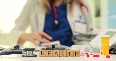 Doktor, ultrason görüntülerini analiz ederek sağlığın korunmasının hastalara olan önemini açıklıyor. Minyatür tahta küpler masada kelime sağlığı oluşturur. Yavaş çekim