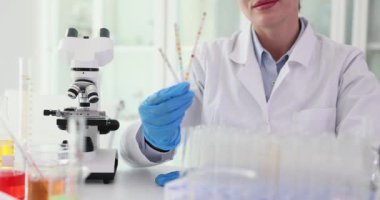 Kadın bilim adamı laboratuvar işyerinde renk çizelgesi gösteriyor. Kadın sıhhiyeci, laboratuvarda yavaş çekimde mikroskop yakınında sıvı araştırmaları yapar.