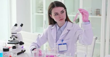 Kimya öğrencisi deney sırasında deney tüpünü sıvı ile gözlemler. Kadın donanımlı tıp merkezinde mor sıvı örneği tutuyor.