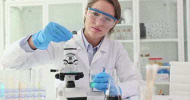 Laboratuvar teknisyeni mikroskop standındaki Petri kabına reaktör eklemiş. Kadın asistan bilimsel ekipmanlarla laboratuarda deney yapıyor.