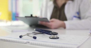 Doktor, masada oturan hasta kayıtlarını kontrol ediyor. Takvimdeki steteskop klinikteki profesyonel sağlık hizmetleri iş akışını temsil ediyor