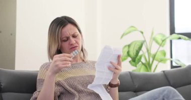 Kadın koltukta oturmuş uzun uyuşturucu talimatlarını endişeli bir ifadeyle okuyor. Reçeteli ilacın beklenmedik yan etkilerinden korkan kadın hasta.
