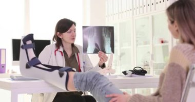 Bayan doktor, bacağı kırık hastaya ayak kemiklerinin röntgenlerini gösteriyor. Travmatolog yaralı kadını iyileşme süreci hakkında bilgilendirdi