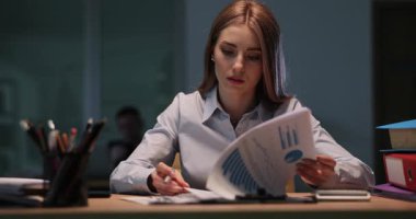 Çalışkan iş kadını masasında oturup mali raporları inceliyor. Odaklanmış ofis çalışanı akşamları karmaşık grafikler ve çizelgeler üzerinde çalışır. Yavaş çekim