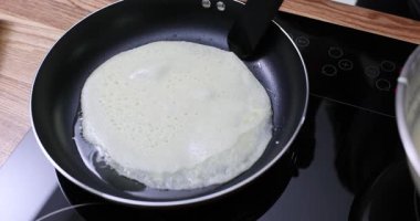 Deneyimli aşçı, tavada spatulayla kızartılmış krep kenarlarını kaldırır. Profesyonel aşçı krep testine hazır olup olmadığını test eder ve takla atmaya çalışır. Yavaş çekim