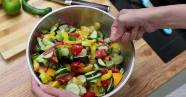 Kadın taze salatayı sebzelerle ve egzotik meyveleri masada metal kasede karıştırıyor. Bayan mutfakta ağır çekimde sağlıklı malzemelerle lezzetli vegan yemekleri pişiriyor.