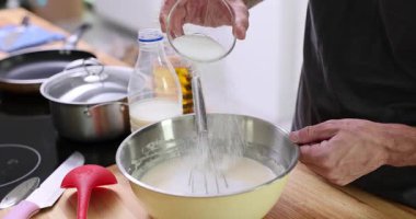 Adam masadaki metal kasede krep hamuruna şeker ekliyor. Erkek, hafif ev mutfağında ev yapımı krep pişiriyor.