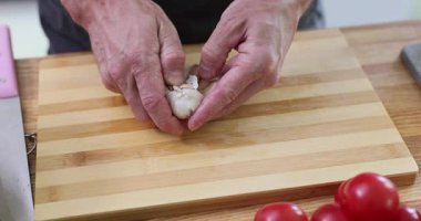 Kırışık eller, sarımsak kafaları odun kesme tahtasından soyar. Erkek aşçı, mutfakta sağlıklı yemek pişirmek için aromatik baharatlı sebze hazırlar.