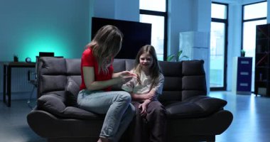 Odadaki kanepede oturan özenli kadın, küçük kızın vücut ısısını ölçüyor. Annem evde bir kızla ilgilenirken ateş hastalığı belirtilerini gösteriyor.