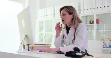 Kadın bir doktor hastalarına yardım etmek için bilgisayarını kullanarak teletıp seansına katılıyor.