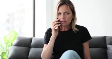 Endişeli bir kadın koltuğunda oturur, telefonda düşünceli bir ifadeyle konuşur, duygularını yansıtır.