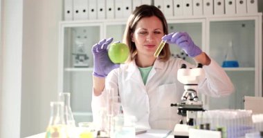 Bilge bir bilim adamı, iyi hazırlanmış bir laboratuvar ortamında test tüpü kullanarak taze bir elmayı dikkatle analiz eder.